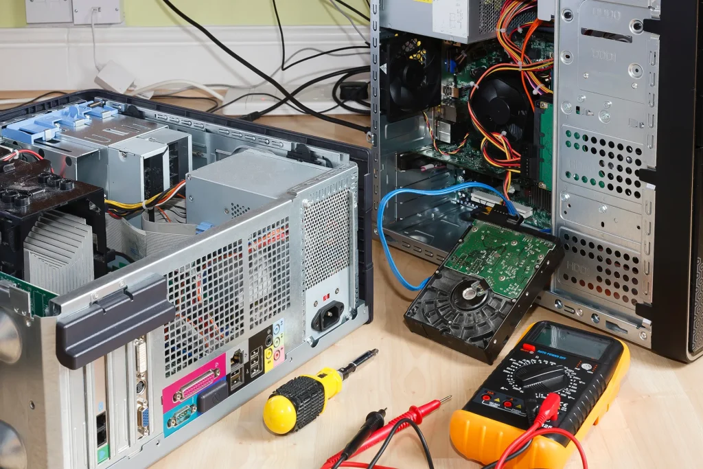 Two open desktop computer towers being serviced, showing the internal hardware, with a hard drive and a multimeter on the desk