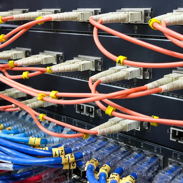 Close-up of a network switch with orange fiber optic patch cables and blue ethernet cables plugged into the ports